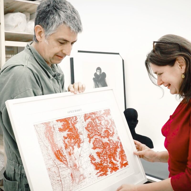 Eine Interessentin betrachtet ein Kunstwerk, das ein Künstler ihr zeigt.